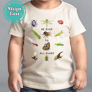 May include: A white t-shirt with a graphic of various insects and the text "Be Kind To All Kinds".