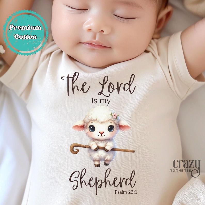 May include: A white baby onesie with a brown graphic of a lamb holding a shepherd's staff. The text "The Lord is my Shepherd" and "Psalm 23:1" is printed on the onesie.