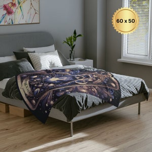 Pode incluir: Uma manta de arremesso azul escuro com um design dourado e branco que apresenta uma carta de tar&ocirc; com a palavra "The Magician" nela. A manta est&aacute; sobre uma cama com almofadas brancas e uma cabeceira cinza. A manta mede 152 cm por 127 cm.