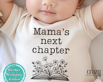 May include: A beige baby onesie with the text "Mama's next chapter" and a black and white illustration of an open book with flowers. The onesie is made of Gerber Premium Cotton.