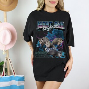 May include: Black t-shirt with a retro graphic design featuring a group of opossums in a teacup. The graphic includes the text "Night Owl Original" in a colorful, 80s-style font.