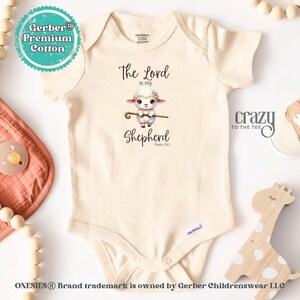 May include: A white Gerber onesie with a cute cartoon lamb holding a shepherd's staff. The onesie has the text "The Lord is my Shepherd Psalm 23:1" printed on it.