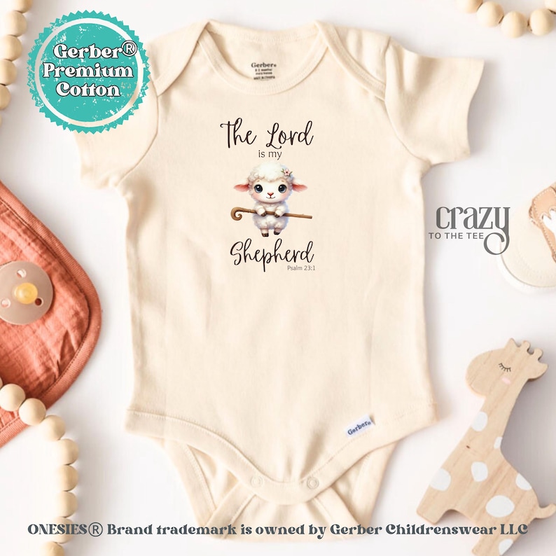 May include: A white Gerber onesie with a cute cartoon lamb holding a shepherd's staff. The onesie has the text "The Lord is my Shepherd Psalm 23:1" printed on it.