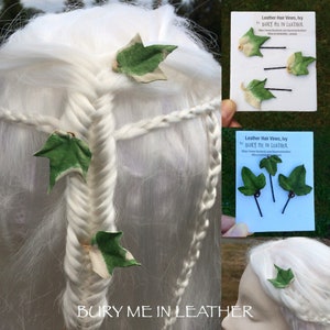 May include: Three leather ivy leaf hair vines with green and white painted details. The vines are attached to gold bobby pins. The image shows the vines on a white wig and on a white card with the text "Leather Hair Vines, Ivy by BURY ME IN LEATHER".