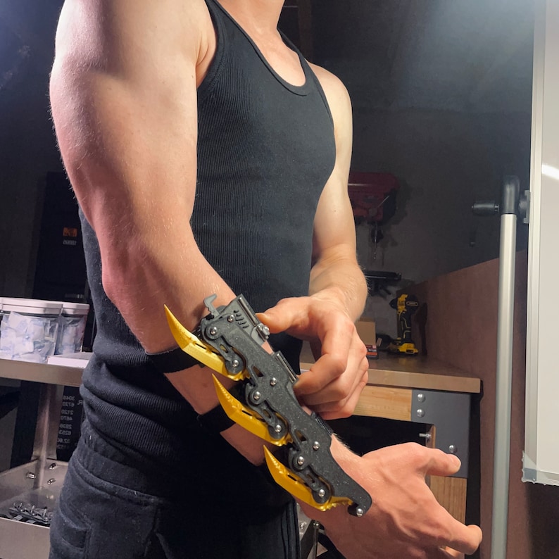 Puede incluir: Una persona con un tanque negro y un dispositivo articulado en forma de garra impreso en 3D, amarillo y negro, en su brazo.