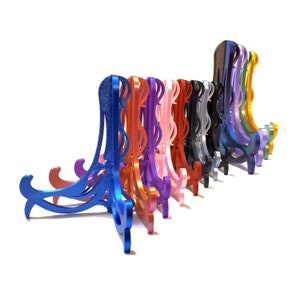 May include: A collection of colorful display stands in various shades, including blue, orange, pink, and black. Each stand has an ornate, curved design and is made of a shiny material. The stands are arranged in a row against a white background.