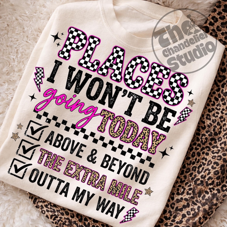 May include: Cream-colored sweatshirt with the text "PLACES I WON'T BE GOING TODAY" in black, pink, and leopard print. The design includes lightning bolts, stars, and checkmarks. The sweatshirt is folded on a leopard print fabric.