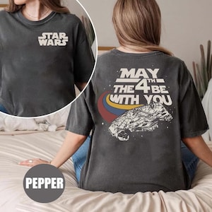Può includere: Una maglietta grigia scura con il testo "STAR WARS" sul davanti e "MAY THE 4TH BE WITH YOU" sul retro. Il retro presenta anche una grafica di un'astronave.