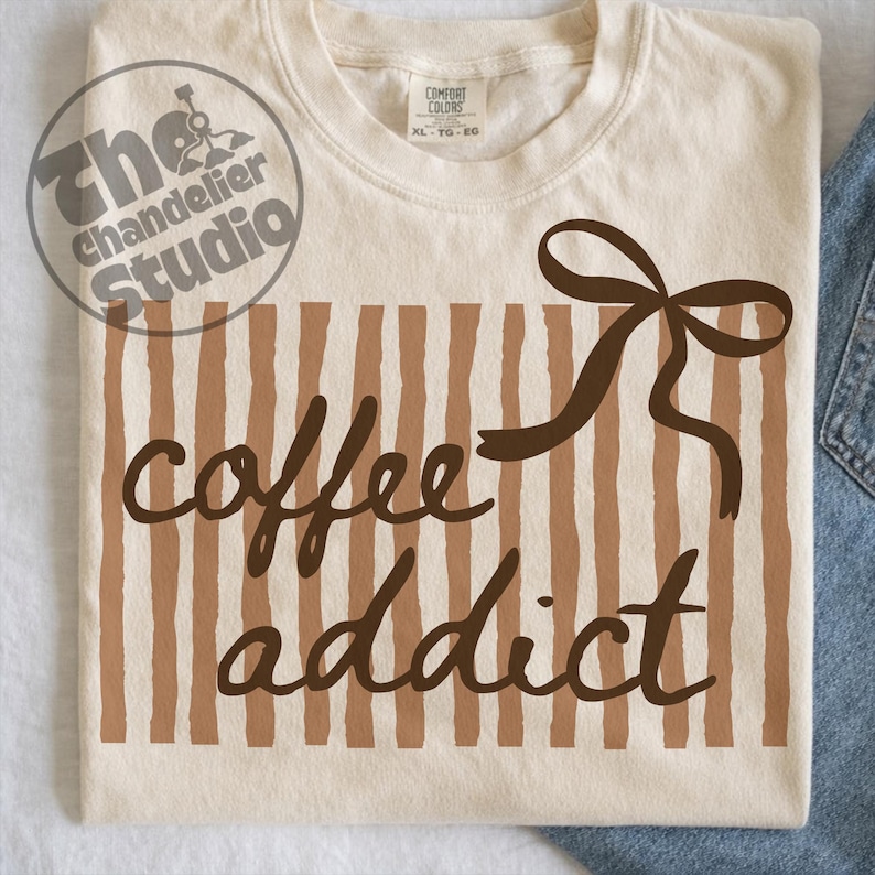 May include: Cream-colored t-shirt with a brown vertical striped pattern and the words "coffee addict" in a brown script font. A brown bow is at the top right. The shirt is a Comfort Colors XL.