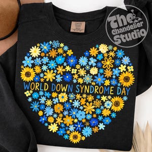 May include: Black sweatshirt with a heart-shaped floral design in yellow and blue. The text "WORLD DOWN SYNDROME DAY" is printed in blue. The sweatshirt has a crew neck and a tag that says "Comfort Colors".