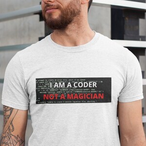 Pode incluir: Uma camiseta branca com um gráfico preto e vermelho que diz "I AM A CODER NOT A MAGICIAN" com texto semelhante a código que envolve as palavras.