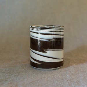 May include: A white and brown ceramic cup with a swirling pattern. The cup is made of pottery and has a smooth, glossy finish.