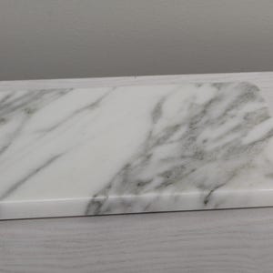 May include: A white marble serving tray with gray veining. The tray has a smooth, polished surface and rounded edges.