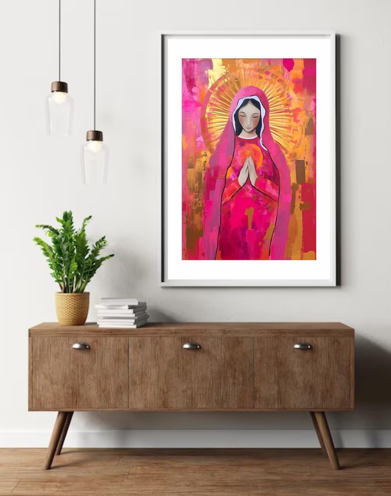 May include: A painting of a woman in a pink robe with a halo of light around her head. She is holding her hands together in prayer. The background is a mix of pink, gold, and white.