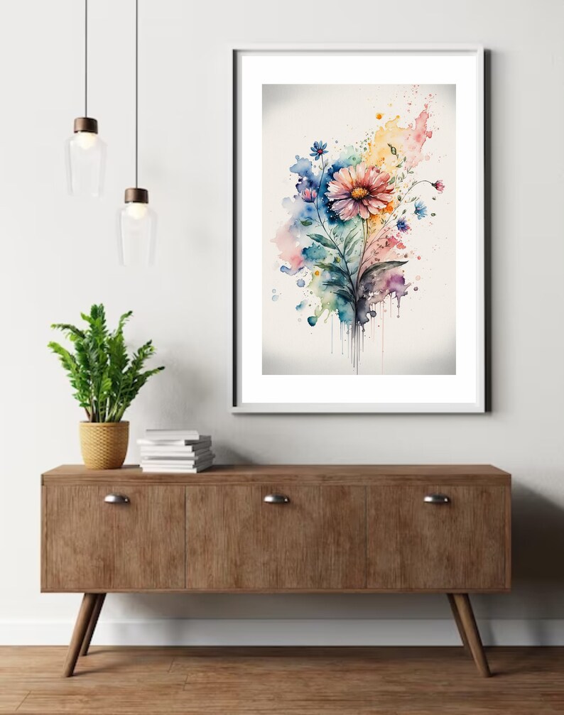 May include: A watercolor painting of a colorful flower bouquet with pink, blue, yellow, and green hues. The flowers are arranged in a loose, organic style, and the background is a soft, white wash. The painting is framed in a white frame and is hanging on a white wall.