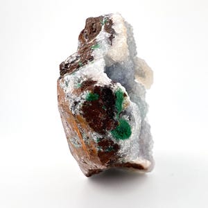 Puede incluir: Un esp&eacute;cimen de geoda natural con un exterior marr&oacute;n rugoso y un interior cristalino. La geoda presenta parches de cristales verdes vibrantes y blancos, con un tono azul claro en el centro. La forma general es irregular y org&aacute;nica.