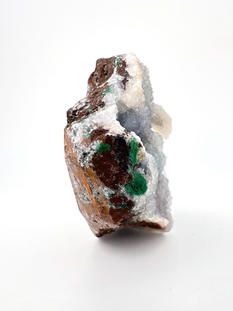 Puede incluir: Un esp&eacute;cimen de geoda natural con un exterior marr&oacute;n rugoso y un interior cristalino. La geoda presenta parches de cristales verdes vibrantes y blancos, con un tono azul claro en el centro. La forma general es irregular y org&aacute;nica.