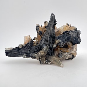 May include: A cluster of black tourmaline crystals with clear quartz crystals. The tourmaline crystals are long and slender, while the quartz crystals are more rounded. The crystals are arranged in a random, natural formation.