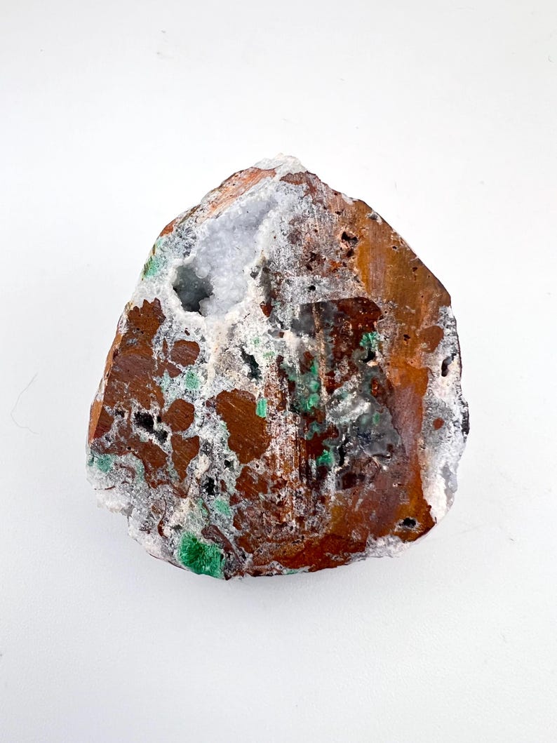 Puede incluir: Una geoda &aacute;spera, marr&oacute;n y blanca con una cavidad llena de cristales blancos e inclusiones verdes.