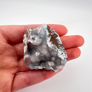 Puede incluir: Un cristal blanco y gris con un exterior marr&oacute;n y verde. El cristal tiene una superficie rugosa y texturizada y es una formaci&oacute;n natural.