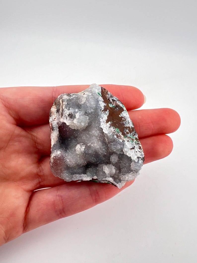 Puede incluir: Un cristal blanco y gris con un exterior marr&oacute;n y verde. El cristal tiene una superficie rugosa y texturizada y es una formaci&oacute;n natural.