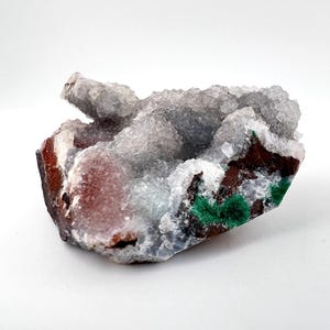 Puede incluir: Un c&uacute;mulo de cristales blancos transl&uacute;cidos con una base marr&oacute;n rojiza y acentos verdes. Los cristales tienen una superficie rugosa y texturizada.