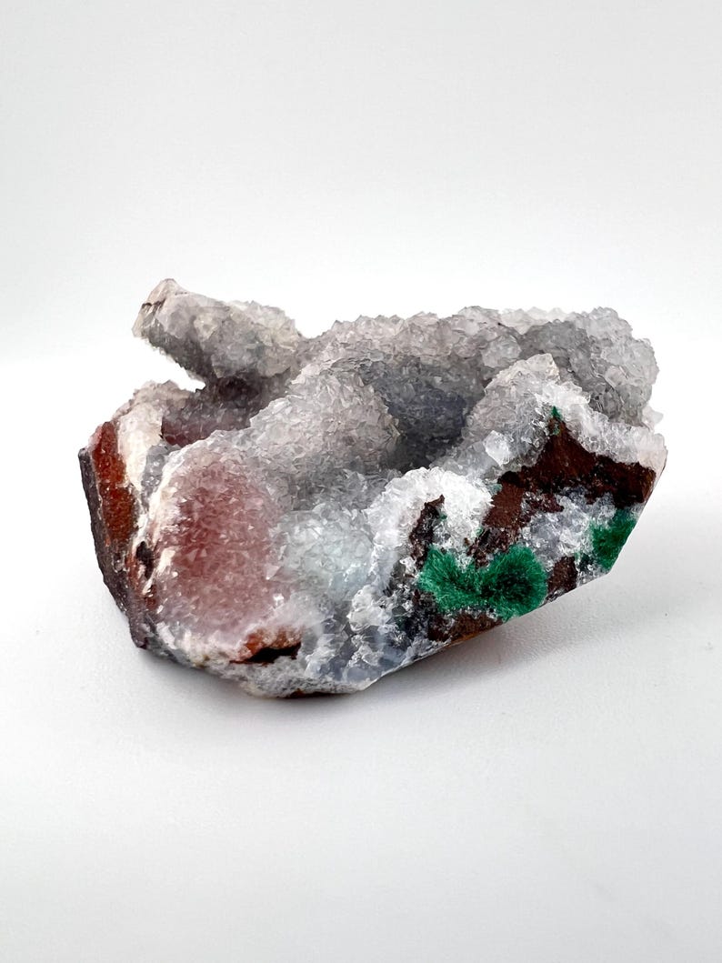 Puede incluir: Un c&uacute;mulo de cristales blancos transl&uacute;cidos con una base marr&oacute;n rojiza y acentos verdes. Los cristales tienen una superficie rugosa y texturizada.