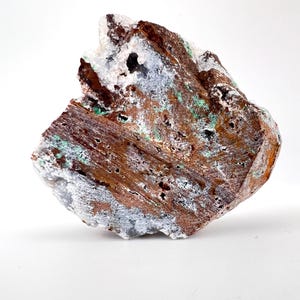 Puede incluir: Esp&eacute;cimen mineral natural en bruto con una superficie rugosa y texturizada. La roca presenta una mezcla de tonos marrones, blancos, grises y verdes. El mineral tiene un aspecto poroso con peque&ntilde;os agujeros y una estructura cristalina.