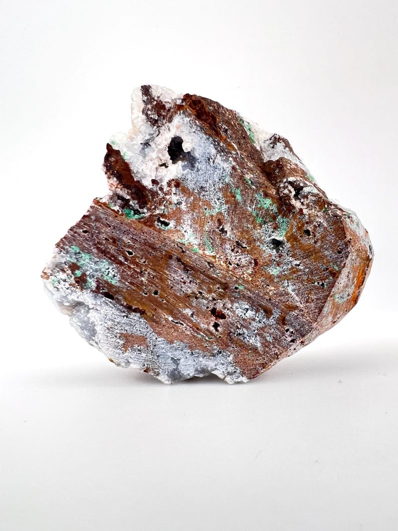 Puede incluir: Esp&eacute;cimen mineral natural en bruto con una superficie rugosa y texturizada. La roca presenta una mezcla de tonos marrones, blancos, grises y verdes. El mineral tiene un aspecto poroso con peque&ntilde;os agujeros y una estructura cristalina.