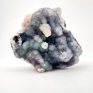 Puede incluir: Un grupo de cristales de cuarzo drusa en tonos de azul, verde y blanco. La formaci&oacute;n cristalina tiene una superficie rugosa y texturizada y se encuentra sobre un fondo blanco. El esp&eacute;cimen mineral muestra una forma natural y org&aacute;nica.