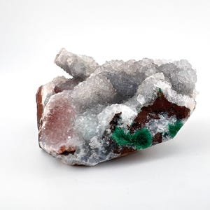 Puede incluir: Un c&uacute;mulo de cristales blancos, grises y rosados con un acento de malaquita verde. Los cristales est&aacute;n agrupados en una forma natural y rugosa.