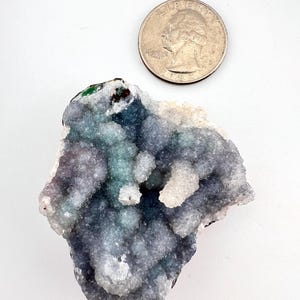 Puede incluir: Un grupo de formaciones cristalinas azules, verdes y blancas. Los cristales tienen una textura burbujeante y est&aacute;n junto a una moneda de veinticinco centavos para comparar el tama&ntilde;o. Los cristales est&aacute;n sobre un fondo blanco.