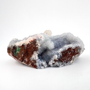 Puede incluir: Una geoda con un interior azul claro y un exterior marr&oacute;n rugoso. La geoda tiene una estructura cristalina y una peque&ntilde;a formaci&oacute;n de cristales blancos en la parte superior. Los bordes muestran toques de verde y rojo.
