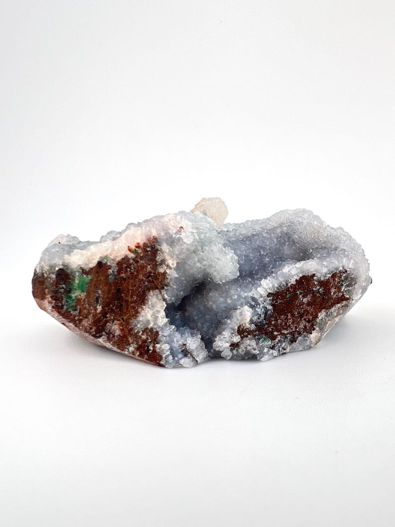 Puede incluir: Una geoda con un interior azul claro y un exterior marr&oacute;n rugoso. La geoda tiene una estructura cristalina y una peque&ntilde;a formaci&oacute;n de cristales blancos en la parte superior. Los bordes muestran toques de verde y rojo.