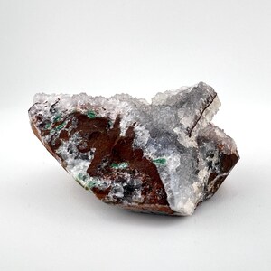 Puede incluir: Un c&uacute;mulo de cristales blancos transl&uacute;cidos con una matriz marr&oacute;n, verde y negra. Los cristales est&aacute;n agrupados en una forma irregular y rugosa.