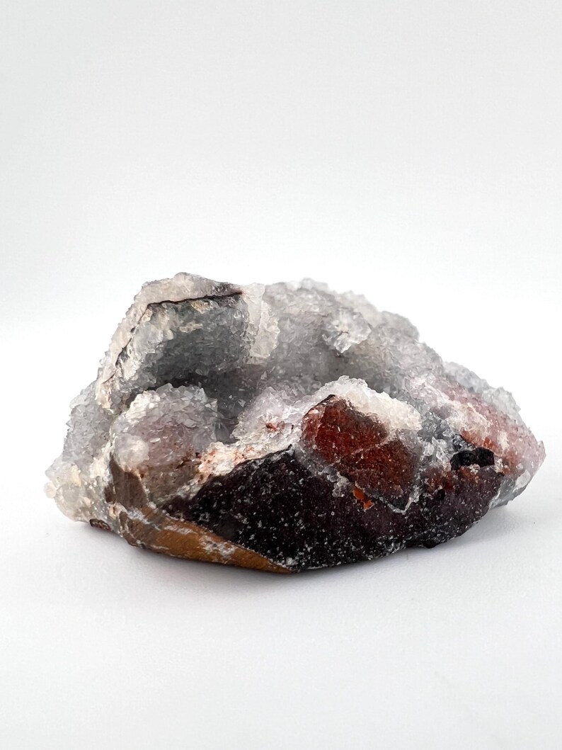 Puede incluir: Un c&uacute;mulo de cristales blancos transl&uacute;cidos con una base marr&oacute;n rojiza. Los cristales tienen una textura rugosa y natural.