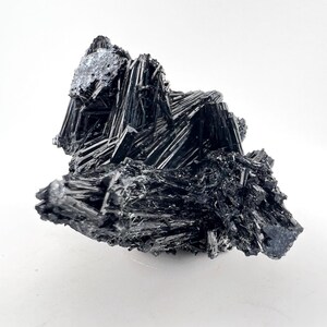 May include: A cluster of black, needle-like crystals with a metallic sheen. The crystals are arranged in a random, organic pattern.