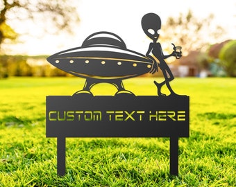 May include: Black metal garden sign depicting a UFO and an alien with a drink. The sign has the text "CUSTOM TEXT HERE" in yellow. The sign is set in a grassy garden.