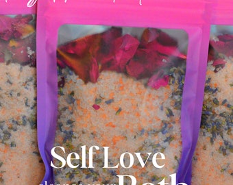 May include: A purple and pink pouch with a clear window showing a bath salt blend with dried rose petals and lavender. The pouch has a white label that reads "Self Love Bath cleanse your energy detox your aura" and "Freyja Phoenix Tarot".