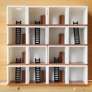 Può includere: Un modello architettonico in miniatura con sedici cubi bianchi. Ogni cubo presenta un pavimento marrone, una porta marrone e una scala nera o uno sgabello nero. Lo sfondo è una superficie di legno marrone chiaro.