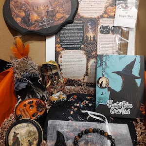 May include: A Samhain-themed gift box containing a Blessed Samhain wooden sign, a Haunted Echoes oracle deck, a jar of dried botanicals, a candle with a Samhain label, a black bird figurine, a beaded bracelet, and a small bag labeled Vampire Blood.