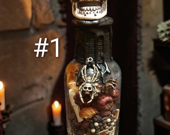 May include: A clear glass bottle filled with various dried botanicals, spices, and small white spheres, topped with a cream-colored skull stopper. The neck is sealed with black wax, and a silver-toned spider charm is attached. The text #1 is visible.