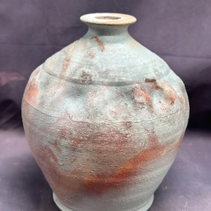 Könnte beinhalten: Eine Keramikvase mit rundem Körper und einer weiten Öffnung. Die Vase ist in einem hellblauen Ton mit braunen und orangen Akzenten glasiert.