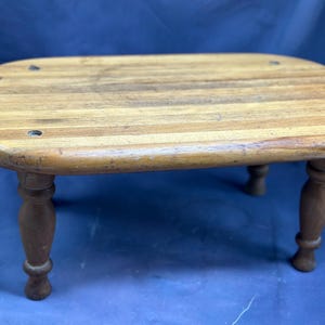 May include: A wooden stool with a rounded top and four turned legs. The top is made of multiple wood strips.