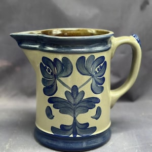 May include: A blue and white ceramic jug with a floral design. The jug has a brown rim and a handle.