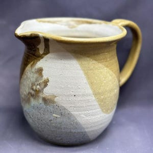 May include: A ceramic pitcher with a brown, white, and blue glaze. The pitcher has a rounded body and a handle.