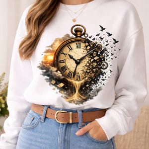 Puede incluir: Una sudadera blanca de manga larga con un estampado gráfico de un reloj de bolsillo dorado con números romanos. El reloj parece desmoronarse en fragmentos oscuros y arena dorada, rodeado por un cielo al atardecer y una bandada de aves negras.