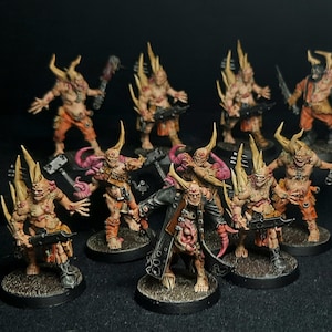 May include: A collection of hand-painted miniature figures, featuring grotesque, horned creatures in various poses. The figures are predominantly flesh-toned with orange accents, and are armed with weapons. The bases are dark, and the background is black.