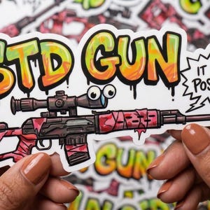 May include: A sticker featuring a cartoon gun with a scope, wrapped in pink and red. The text "STD GUN" is in graffiti-style lettering, and a speech bubble says "IT WENT POSITIVE!"