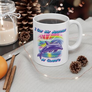 May include: White ceramic coffee mug with a purple dolphin jumping over a rainbow with the text "I got my abortion at Claire's" printed on the front.